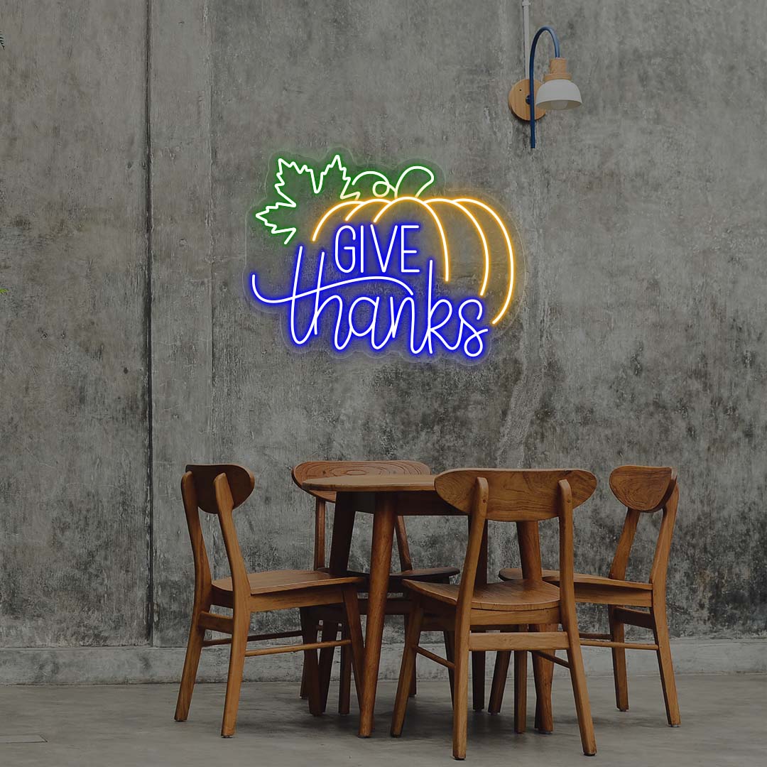 Give Thanks neon sign with pumpkin and green leaf, blue and orange lights, Thanksgiving wall decor above wooden dining table