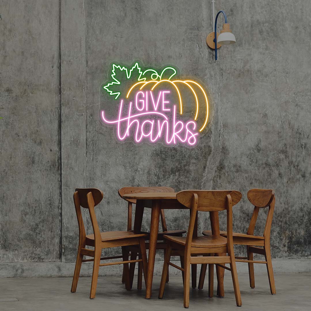 Give Thanks neon sign with pumpkin and green leaf, pink and orange lights, Thanksgiving wall decor above wooden dining table