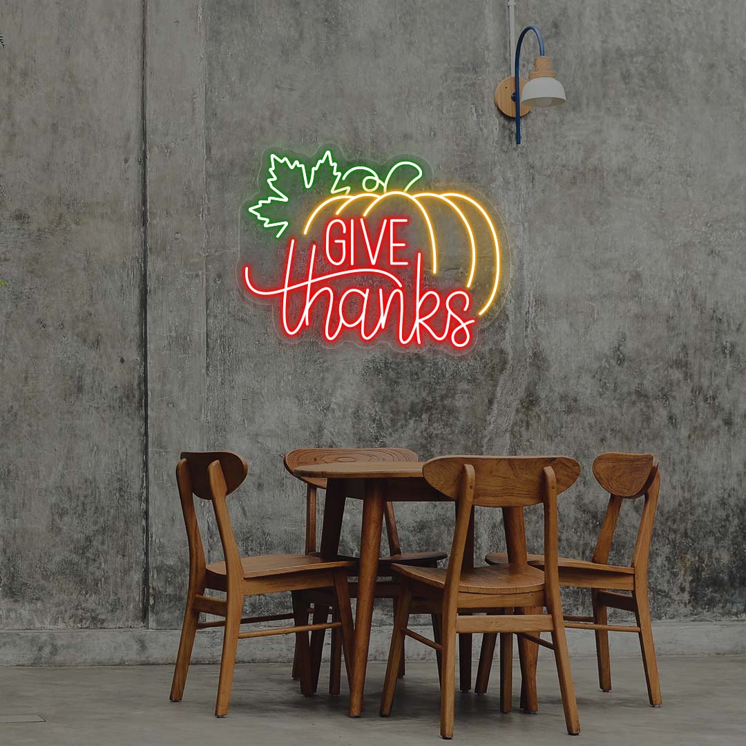 Give Thanks neon sign with pumpkin and green leaf, red and orange lights, Thanksgiving wall decor above wooden dining table