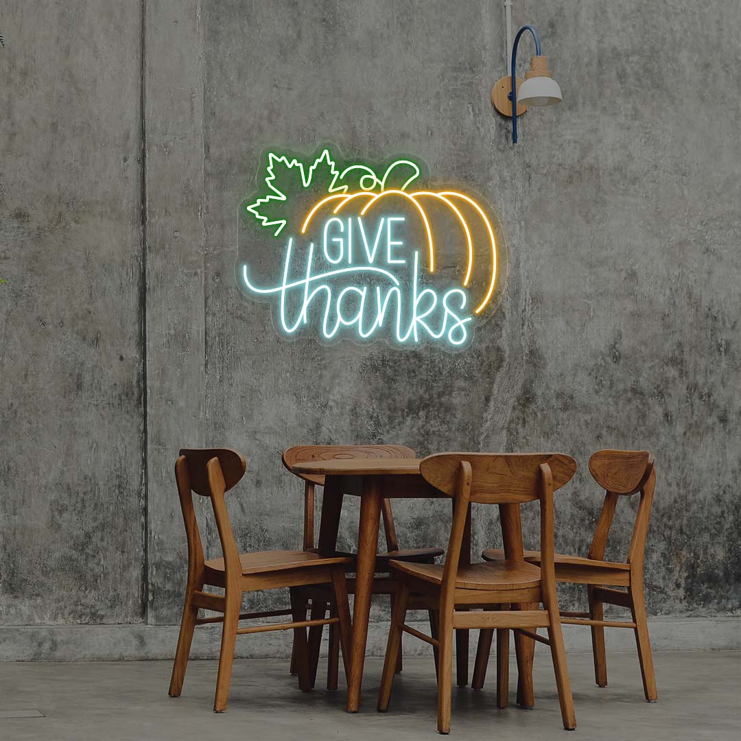 Give Thanks neon sign with pumpkin and green leaf, iceblue and orange lights, Thanksgiving wall decor above wooden dining table