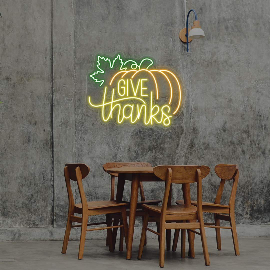 Give Thanks neon sign with pumpkin and green leaf, yellow and orange lights, Thanksgiving wall decor above wooden dining table