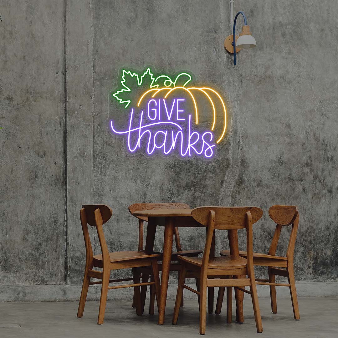 Give Thanks neon sign with pumpkin and green leaf, purple and orange lights, Thanksgiving wall decor above wooden dining table