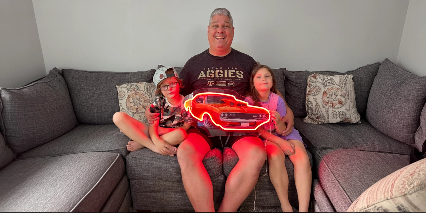 Red car neon sign artwork held by family on grey sectional sofa in modern living room