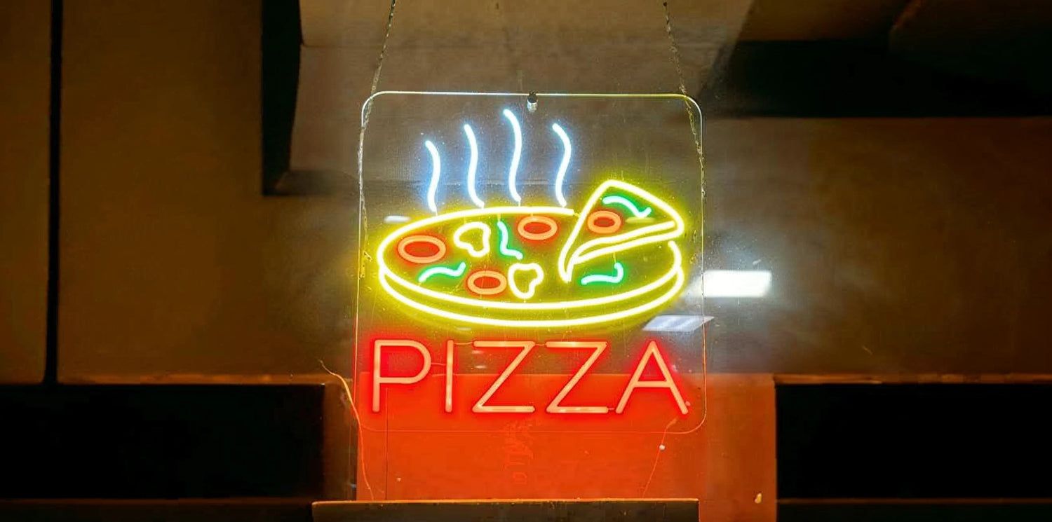 Neon sign with a brightly illuminated image of a pizza slice above the word 'PIZZA' in red letters, hanging against a dark restaurant background.