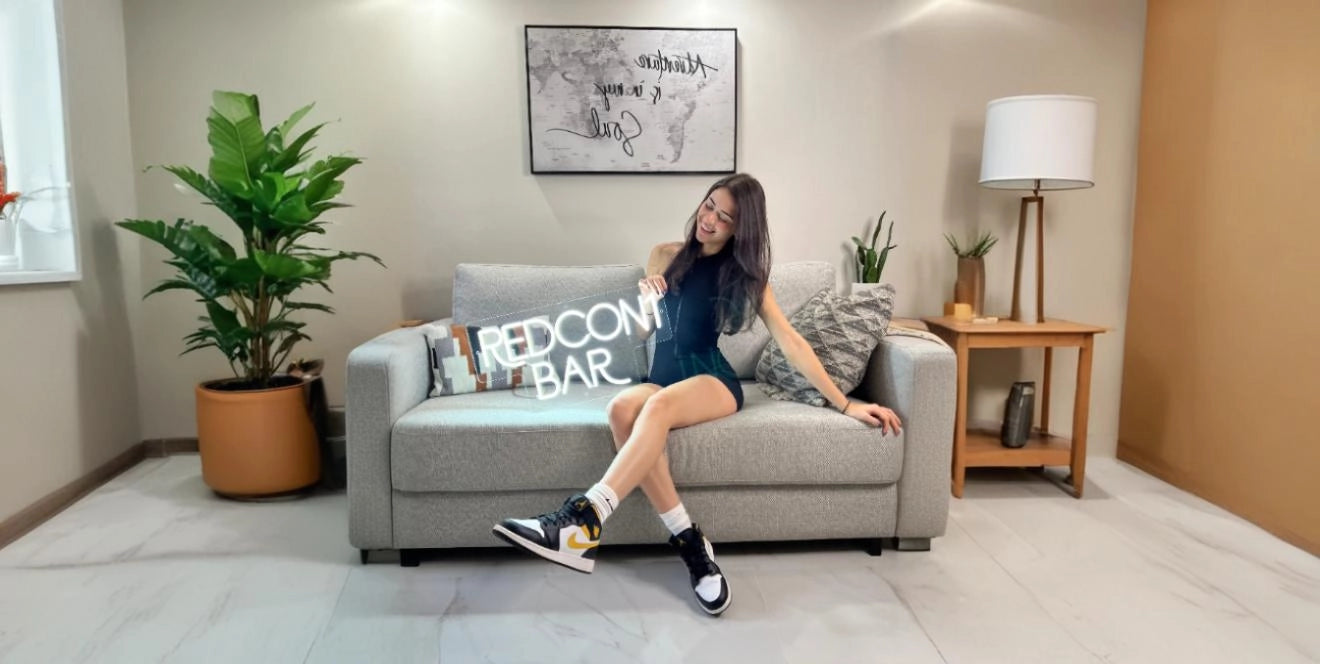 Redcon bar neon sign held by woman sitting on modern grey sofa in stylish living room