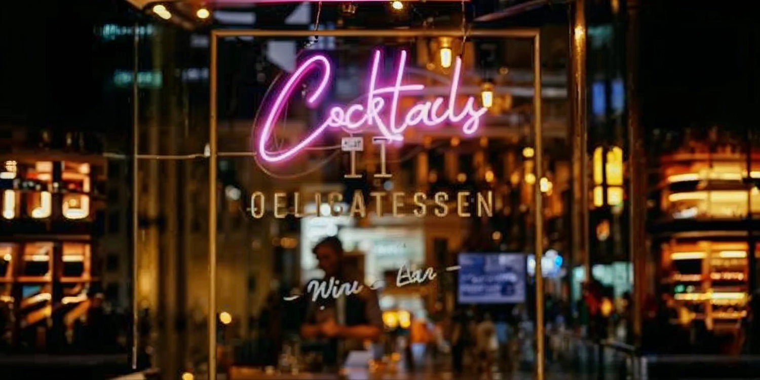 Neon cocktails sign at bar entrance with delicatessen lights in background