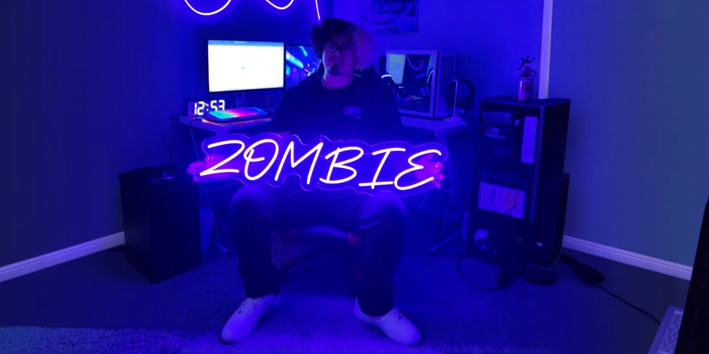 Person sitting in a dark gaming room illuminated by blue neon lights, holding a glowing neon sign that reads 'ZOMBIE' in front of computer screens and gaming equipment