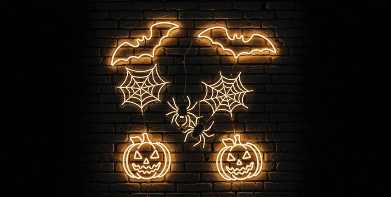Yellow neon Halloween wall art displaying bats, spider webs, spiders, and two jack-o'-lantern pumpkins, glowing against a dark brick background