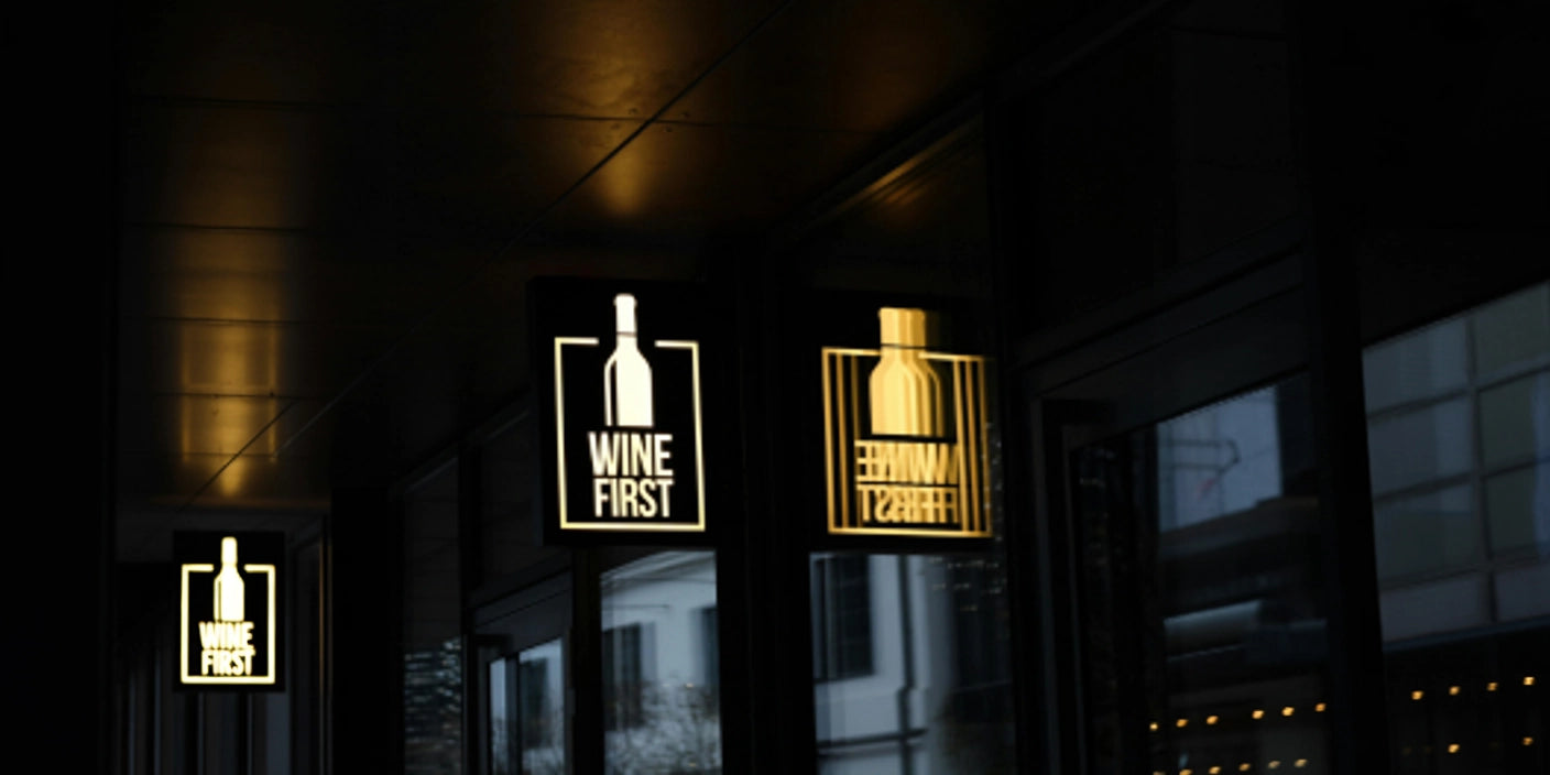 Wine First illuminated bottle logo lightbox sign on modern building exterior at night