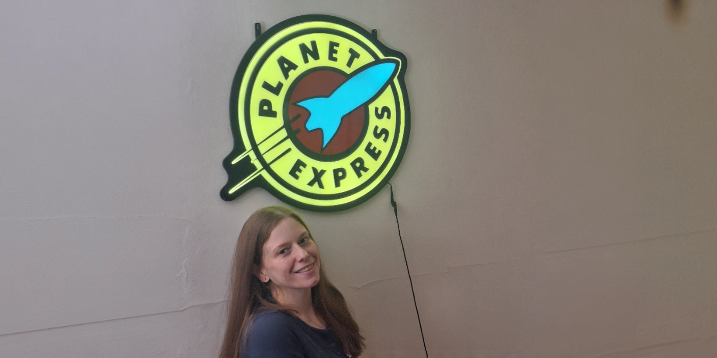 Woman posing under Planet Express lightbox sign with rocket art on minimalist wall