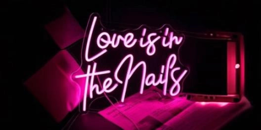 Love is in the Nails pink neon sign glowing in dark nail salon with workspace ambiance