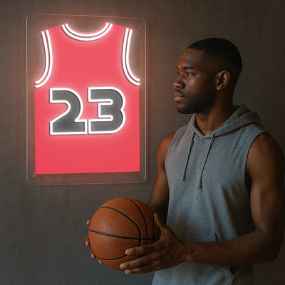 Man holding basketball beside red jersey neon sign with number 23 on wall
