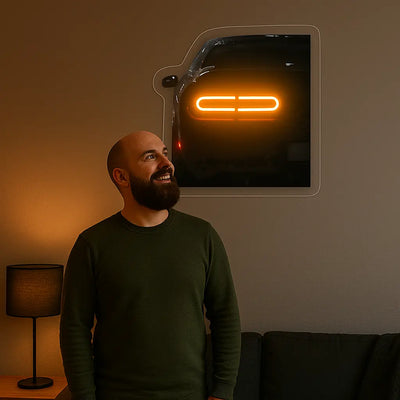Man smiling while looking at car-shaped neon wall light glowing orange in living room