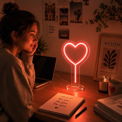 Heart neon lamp glowing on a cozy desk beside a laptop and candle creating a warm romantic atmosphere perfect for relaxing journaling or winding down at home