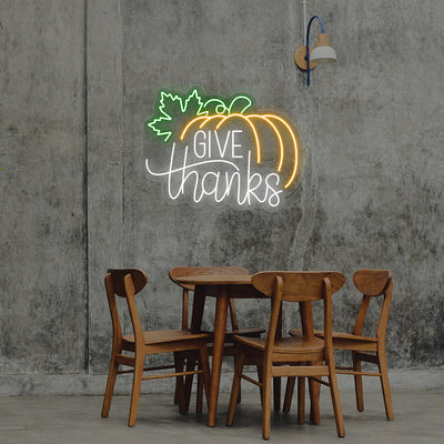 Give Thanks neon sign with pumpkin and green leaf, white and orange lights, Thanksgiving wall decor above wooden dining table