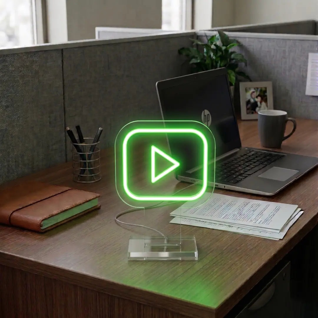 Green Youtube neon sign on a modern office desk beside a laptop, notebook, and workspace essentials in a professional cubicle setting.