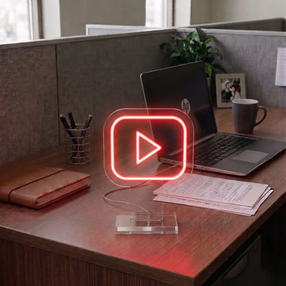 Red Youtube neon sign on a modern office desk beside a laptop, notebook, and workspace essentials in a professional cubicle setting.