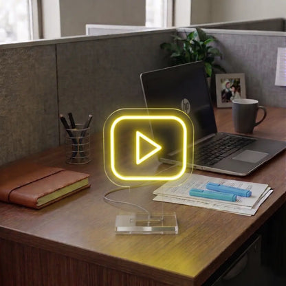 Yellow Youtube neon sign on a modern office desk beside a laptop, notebook, and workspace essentials in a professional cubicle setting.