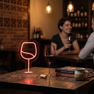 Wine glass neon lamp glowing on a rustic table beside a glass of red wine, creating a warm and inviting atmosphere in a cozy wine bar setting.