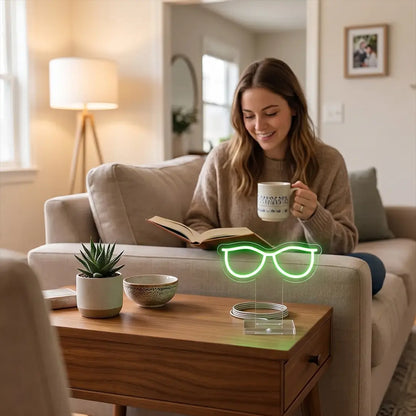 Green glasses neon lamp on a coffee table beside a woman reading on a cozy sofa, adding a playful glow to a warm and relaxing living room.