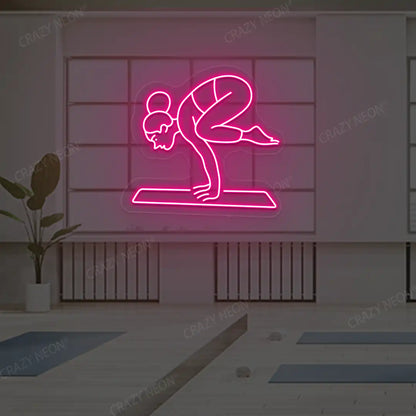 Bakasana Yoga Neon Sign lighting up in pink color in a yoga room