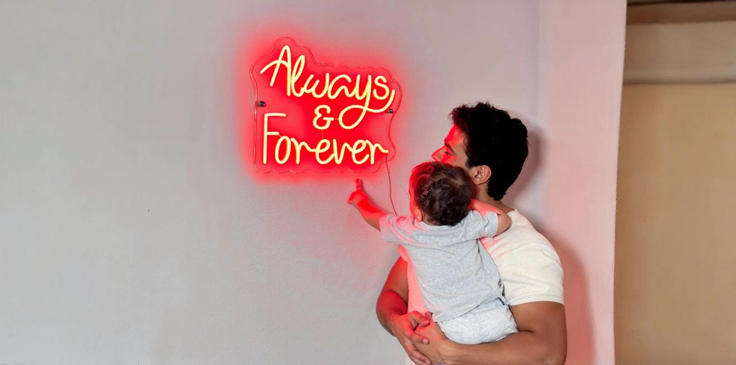 Neon sign reading 'Always & Forever' in glowing red script mounted on a light wall, with an adult holding a child pointing toward the sign