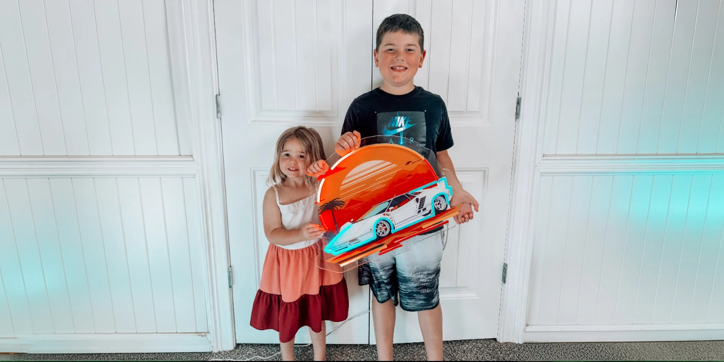 Kids holding sunset sports car neon sign artwork in front of white panel doors