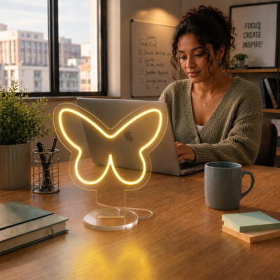 Butterfly Neon Desk Lamp glowing in yellow light on a workspace desk beside a laptop in a modern office.