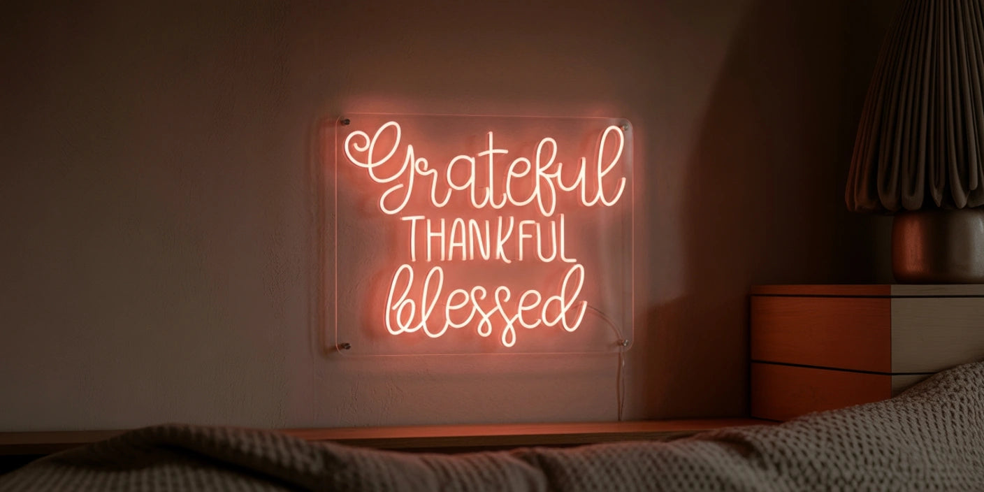 warm pink neon sign reading Grateful Thankful Blessed in cursive script glowing on dark wall in cozy bedding 