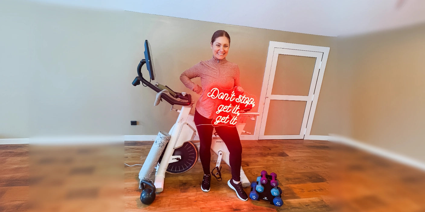 Woman with Don't stop get it neon sign in gym room with exercise bike and colorful dumbbells