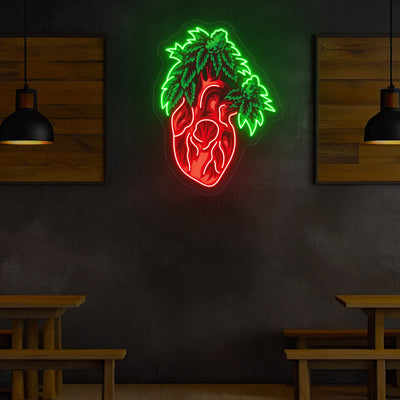 Neon wall art featuring a glowing anatomical heart with bright red tubing and luminous green leaves sprouting from the top displayed on a dark wall