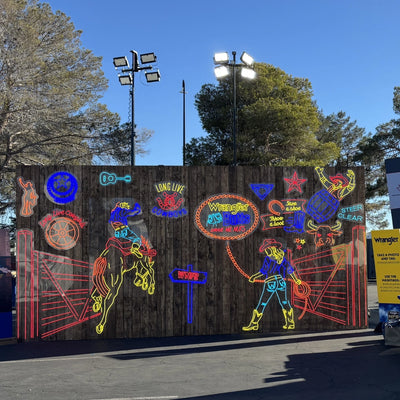 Wrangler rodeo event neon signs on large wooden display wall outdoors, featuring cowboy, bull rider, and western icons