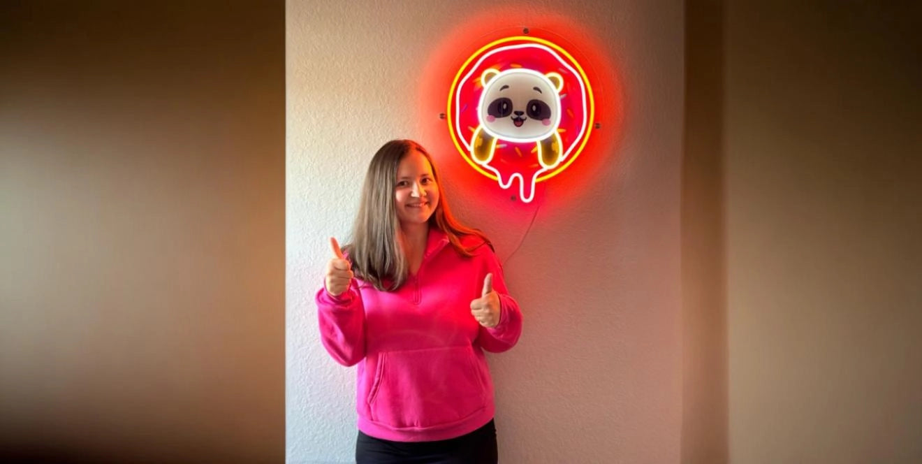Woman in pink sweatshirt giving thumbs up in front of bright panda donut neon LED neon artwork on wall