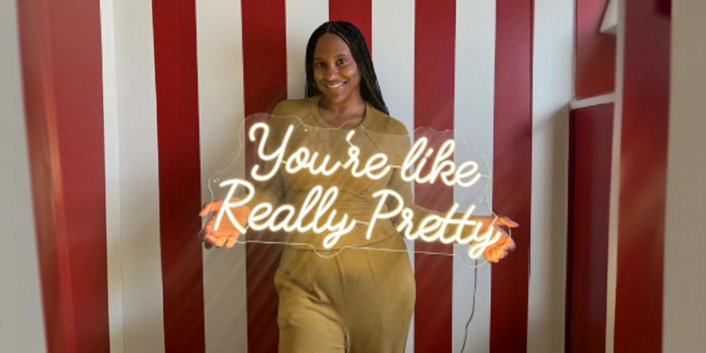 Woman holding You're Like Really Pretty neon sign in front of red and white striped wall