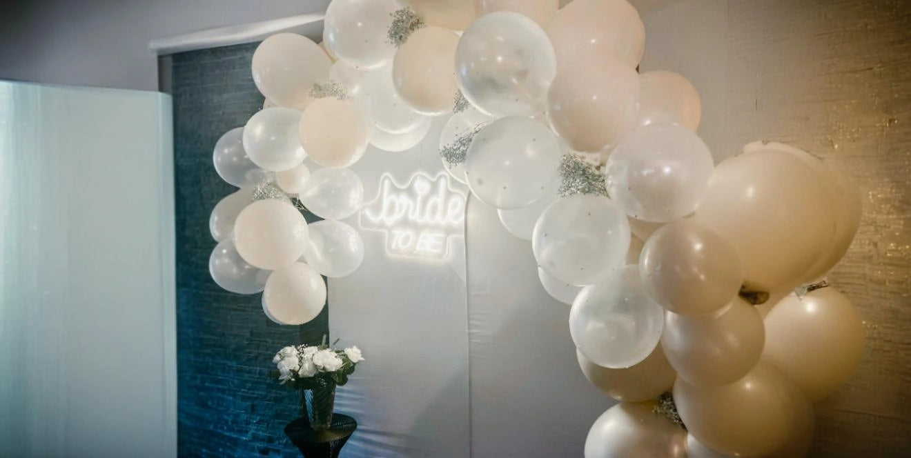 Bride to Be neon sign glowing behind white balloon arch at bridal shower or wedding event