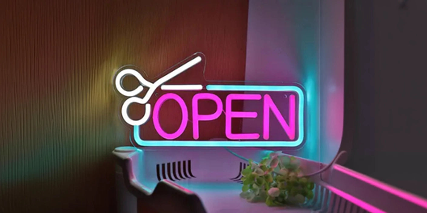 Scissors and open neon sign in pink and white, illuminated on salon counter