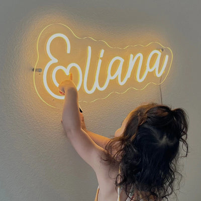 Little girl pointing at custom Eliana yellow neon name sign on wall