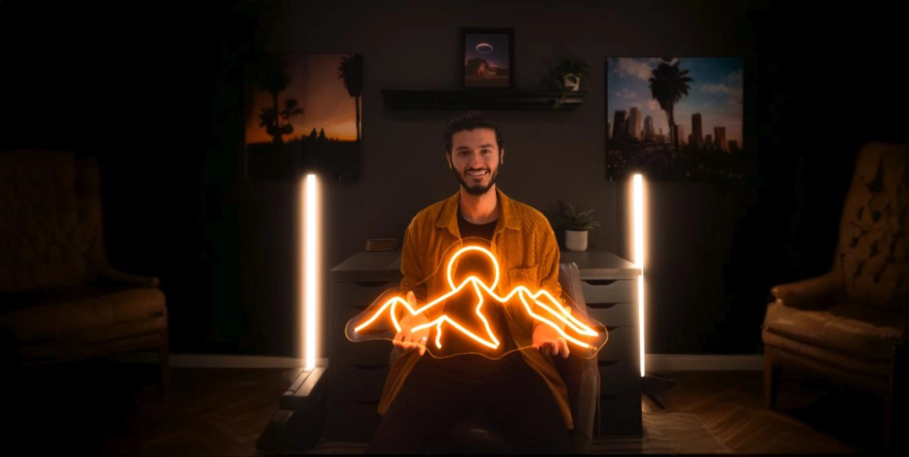 Man holding orange mountain sunrise neon sign in moody modern room with artistic wall decor