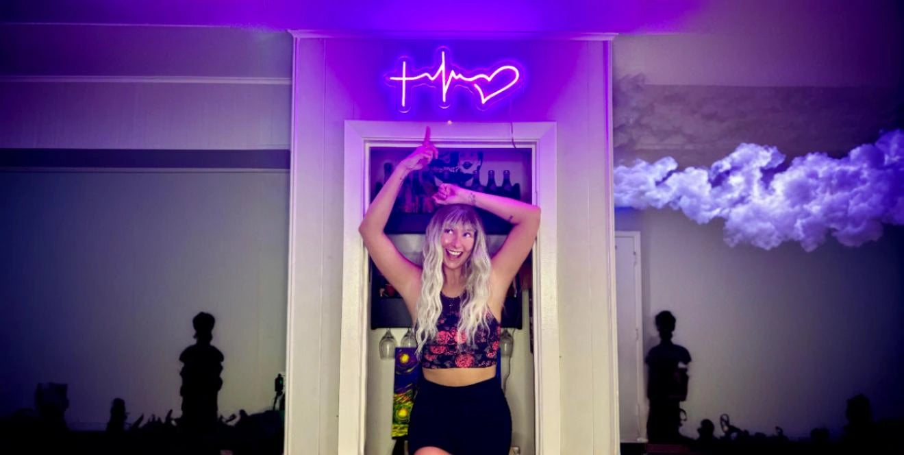 Woman with long blond hair standing under purple heartbeat and heart neon sign in stylish room